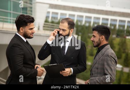 A group of business people meet outdoors. Male employees in suits communicate outdoors. Business partners discuss and argue. Relationships and Stock Photo