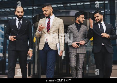 Business people outdoor meeting, A group of male businessmen in suits exit the front door of a glass building. Working break. Teamwork and Stock Photo