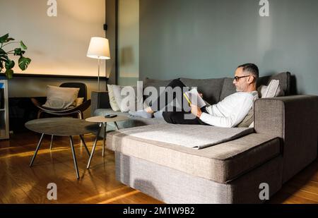 Man reading book on couch. Stock Photo