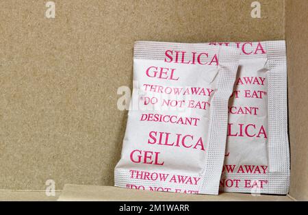 Two Silica gel packets in the bottom corner of a cardboard box. Porous desiccant substance used in packing material to absorb humidity moisture. Stock Photo