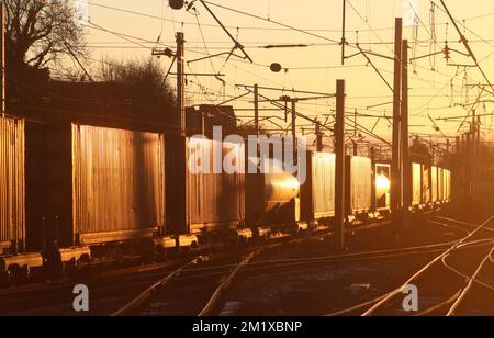 Glint, sunlight reflecting off side of containers of freight train passing Carnforth North junction on West Coast Main Line on 7th December 2022. Stock Photo