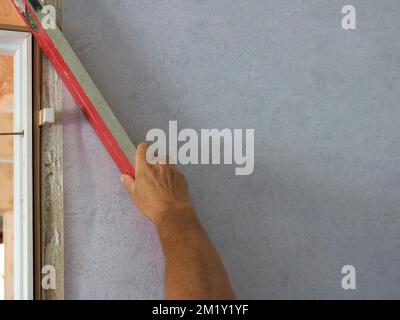 working with a level to check the desired angle during repairs in the room, a man's hand holds a red level and measures the slope of the door frame Stock Photo