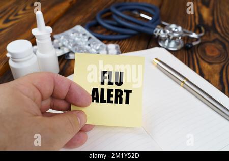 Medical concept. On the table is a notebook, medicines and a stethoscope, in the hands of a sticker with the inscription - Flu alert Stock Photo