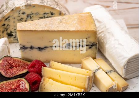 Cheese collection, marble board with French cheeses brie, tomme, matured goat cheese, morbier  served with fresh raspberries and figs close up Stock Photo