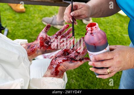 Artificial moulage blood being painted on a pair of hands in simulation of serious injury for a first aid training exercise Stock Photo