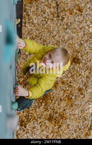 Boy At The Climbing Wall Without A Helmet, Danger At The Climbing Wall. Little Boy Climbing A Rock Wall Indoor Stock Photo