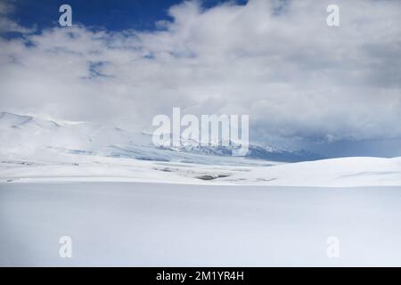 White snowy field with a snow-covered mountain range on the Assy plateau against the background of a sky with thick clouds Stock Photo