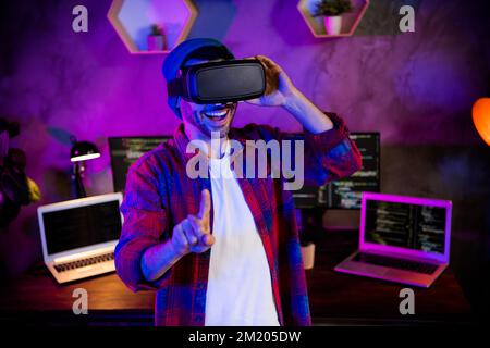 Photo of funny smiling coder dressed hat eyewear teating 3d game modern gadget indoors workplace workstation loft Stock Photo