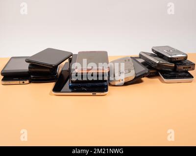 Lots of old smartphones on an orange background. Old mobile phones. Broken smartphones. Stock Photo