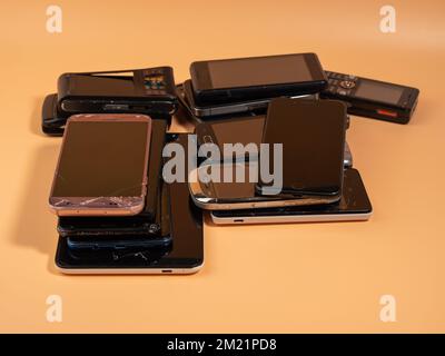 Lots of old smartphones on an orange background. Old mobile phones. Broken smartphones. Stock Photo