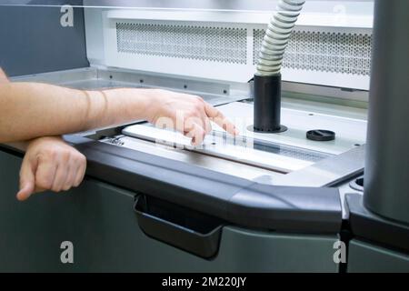 A male worker stands near the powder part of a powder 3D printer and points his finger of the hand at it. industrial production equipment. New modern 3D printing additive progressive technology MJF Stock Photo