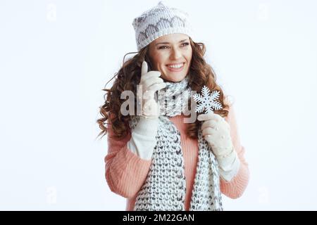 Hello winter. smiling modern woman in sweater, mittens, hat and scarf against white background with snowflake speaking on a smartphone. Stock Photo