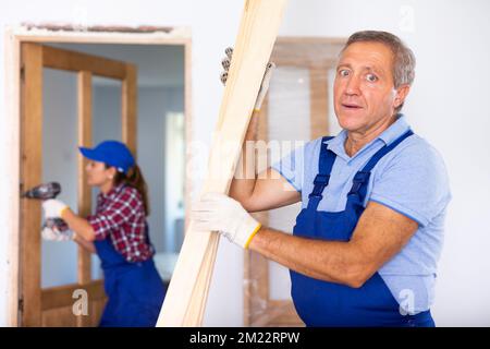 Confident middle-aged repairman in uniform checking wooden timber at a construction site in an apartment Stock Photo