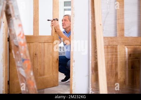 Focused middle-aged repairman checking a doorknob on a door in the house Stock Photo
