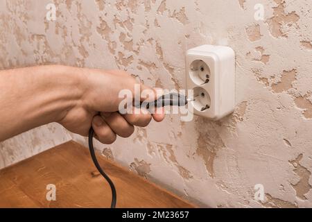 A man hand inserts or removes a plug from an outlet in a modern interior. Safe use of electrical appliances concept. Stock Photo