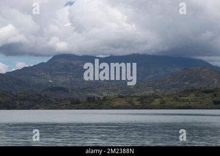 Beautiful andean mountain range with clouds at the top viewed from a lake shore in sunny day Stock Photo