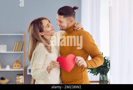 Smiling, happy, beautiful man and woman hugging each other, holding a red heart on Valentine's day. Stock Photo