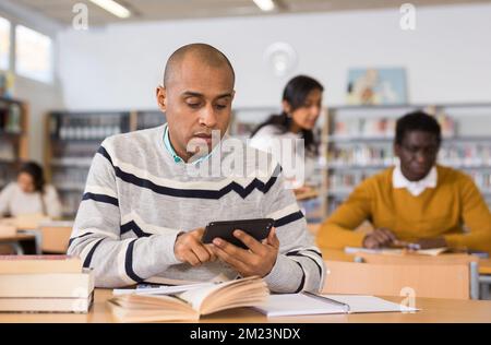 Focused hispanic man using phone in public library Stock Photo