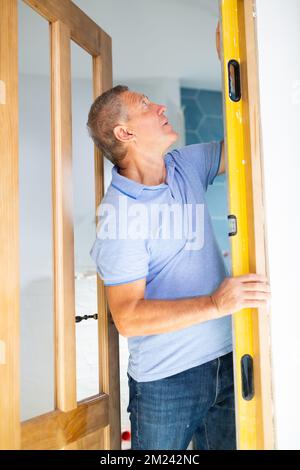 Concentrated male builder using a waterpass on the wooden door of the apartment Stock Photo
