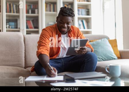 Black businessman sitting at home, looking at screen of tablet Stock Photo