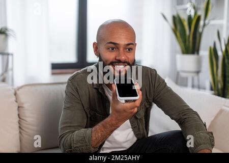 Portrait of positive latin man holding cellphone near mouth recording message talking on smartphone Stock Photo