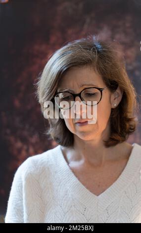 portrait of a 50 year old woman on a dark brown background who looks worried or annoying Stock Photo