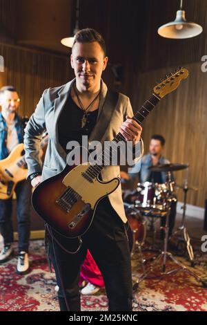 music band guitarist performing repetition with his band in the recording studio,medium-full shot a guitarist and a drummer in the background. High quality photo Stock Photo