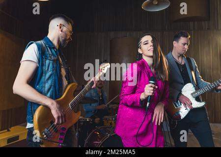 we love our job, a singer girl, two guitarists and a drummer performing for the camera, medium shot. High quality photo Stock Photo