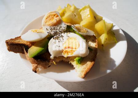 Sliced avocado and egg on toasted bread with bite. Close-up. Stock Photo
