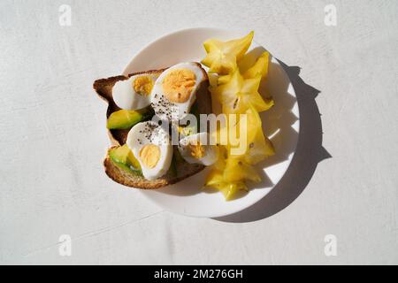 Sliced avocado and egg on toasted bread with carambola for healthy breakfast.  Stock Photo