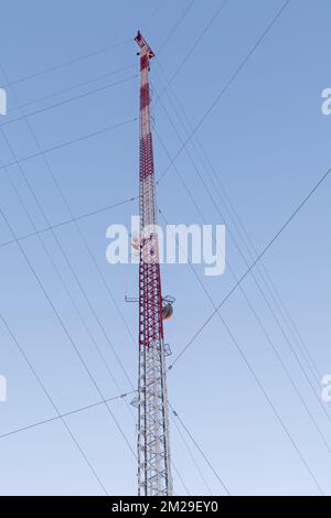 tall wireless communications tower tethered by cables against blue sky Stock Photo