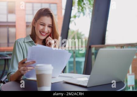 Young businesswoman working with papers and talking on mobile phone, reading financial documents while sitting at cafe. Stock Photo