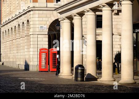 Two old red telephone boxes and colonnaded buildings soon after sunrise at Covent Garden and James Street, London, England Stock Photo