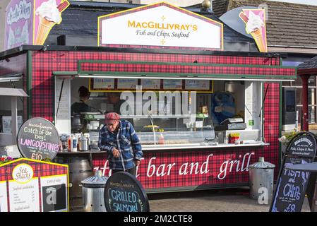 Old man in front of fish & chips and seafood stand in the city Oban, Argyll and Bute, Scotland, UK | Etal de fish and chips dans le port de la ville Oban, Argyll and Bute, Ecosse, Royaume-Uni 05/06/2017 Stock Photo