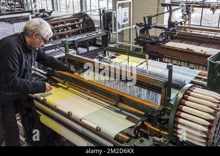 Fabric weaver operating mechanical flying shuttle loom / shuttle weaving machine in cotton mill / spinning-mill | Métier à tisser mécanique dans filature cotonnière 11/02/2018 Stock Photo