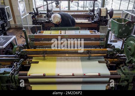 Fabric weaver operating mechanical flying shuttle loom / shuttle weaving machine in cotton mill / spinning-mill | Métier à tisser mécanique dans filature cotonnière 11/02/2018 Stock Photo