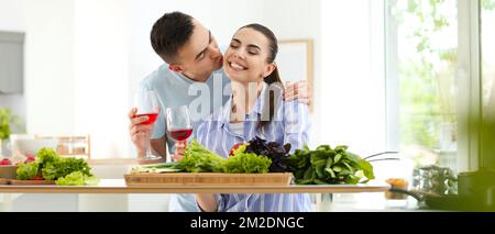 Happy young couple drinking wine while cooking together in kitchen Stock Photo