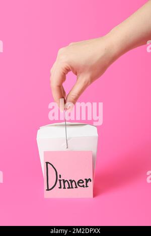 Woman holding box with Asian food and sticky note with word DINNER on color background Stock Photo