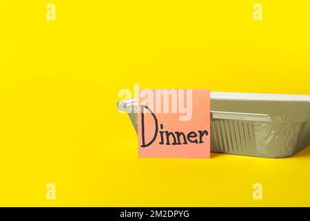 Takeaway box and sticky note with word DINNER on color background Stock Photo