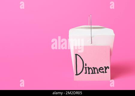 Box with Asian food and sticky note with word DINNER on color background Stock Photo