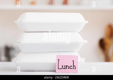 Food containers and sticky note with word LUNCH on white table Stock Photo