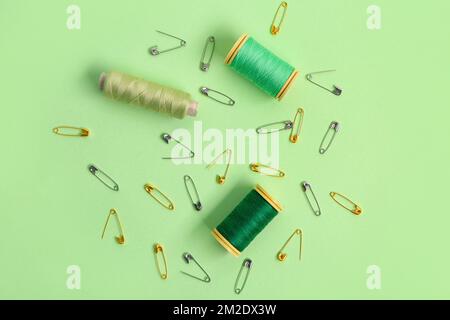 Thread spools and safety pins on green background Stock Photo