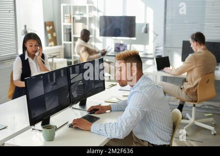 Side view portrait of Asian young man looking at surveillance camera feed in security center with people working Stock Photo