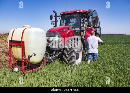A tractor with a trailed sprayer sprays the field with a targeting fungicidal treatment - getting in the tractor | Un tracteur pulverise son champ a l'aide d'un traitement fongicide traitant certaines maladies fongiques sur la production - Monter dans le tracteur 08/05/2018 Stock Photo