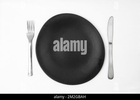 irregular round black plate with silver fork and knife on white background Stock Photo