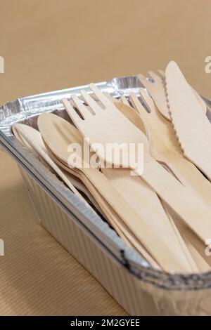 Wooden takeaway cutlery, knife fork spoon, in foil tray containers on brown paper. Disposable biodegradable plastic free takeaway items Stock Photo