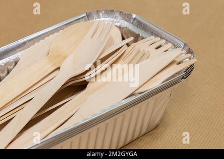 Wooden takeaway cutlery, knife fork spoon, in foil tray containers on brown paper. Disposable biodegradable plastic free takeaway items Stock Photo