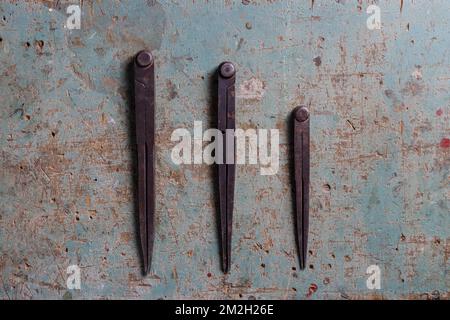 Three metal compass dividers for woodworking on a rustic surface flat lay top view Stock Photo