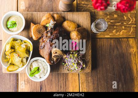 Top view of Golonka - oven-baked pork knuckle - traditional Polish dish served beautifully on a wooden board with oven-baked crispy potatoes, sauces, and pickles. High quality photo Stock Photo