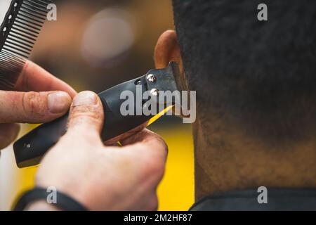 Closeup of an electric razor used by professional barber on his male client. Haircare at barbershop. Back view. High quality photo Stock Photo
